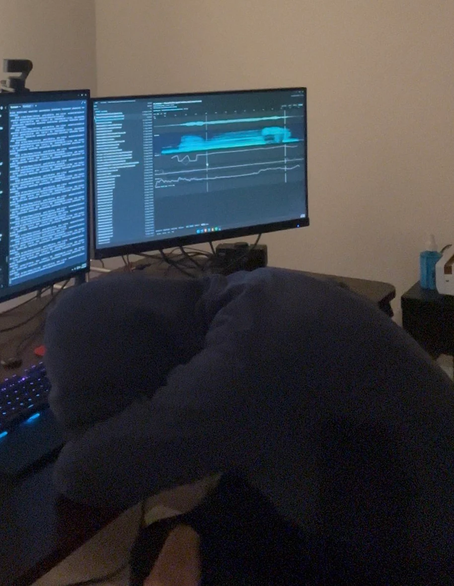 A desk at night with two monitors, source code on one and Performative's pitch display on the other